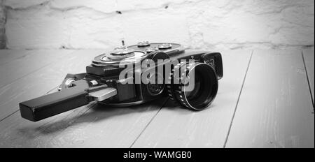 Vintage portable movie film camera on a wooden background. Monochrome Stock Photo