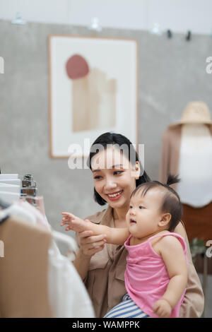 It is not easy to be a working mom! Young beautiful designer  working on her atelier while standing with her baby girl Stock Photo