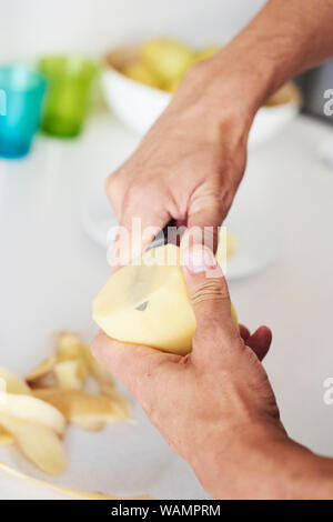 closeup of a caucasian man in the kitchen cutting thin slices of a raw potato with a knife Stock Photo