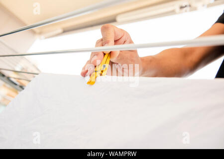 closeup of a young caucasian man hanging wet clothes on a drying rack in a balcony Stock Photo