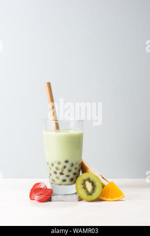 Boba/ buble tea  glass with kiwi, strawberry, orange slices on blue background. Stock Photo