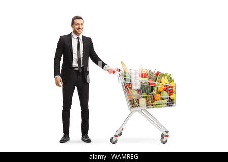 Full length portrait of a businessman posing with a shopping cart with food isolated on white background Stock Photo