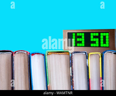 row of books and electronic clock on a blue background Stock Photo