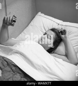 Waking up. A young woman has just been waken up by the sound of the alarm clock. She lies in bed looking at it. Sweden 1946. Photo Kristoffersson ref Y22-4 Stock Photo
