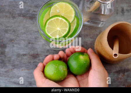 Close up woman hand hold lemons and lime slices for detox water on gray wooden background, a drinking water for healthy diet and skin care Stock Photo