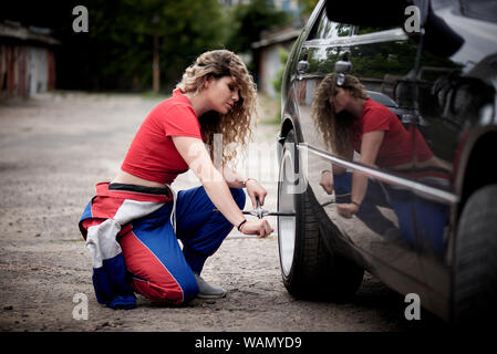 A young woman in overalls on a garage is repairing a auto. Stock Photo