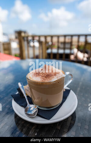 Close up of a cup of coffee in a glass mug, outside in a UK beach holiday resort, Pendine Wales Stock Photo