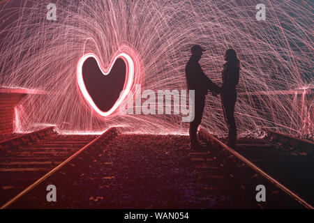 Silhouette of man and woman with sparks behind them in a love heart shape Stock Photo