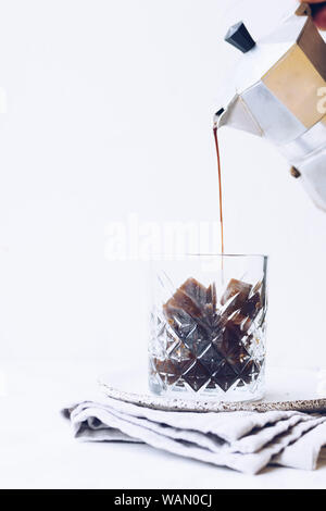 Pouring coffee from a moka to a glass of espresso ice cubes on white background with copy space. Cold summer drink. Stock Photo