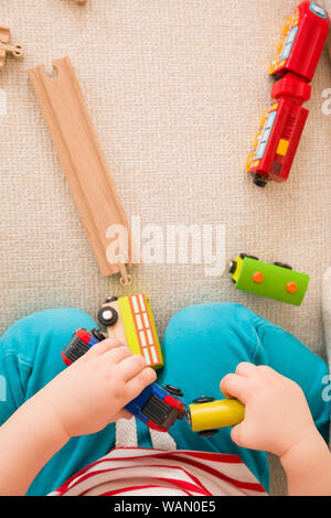 Closeup of child's hands playing with wooden train toys and railway. Top view. Toddler boy sitting and playing with railroad indoors. Developing activ Stock Photo