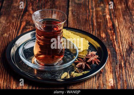 Spiced tea in oriental glass with star anise and green cardamom with navad on metal tray over wooden surface Stock Photo