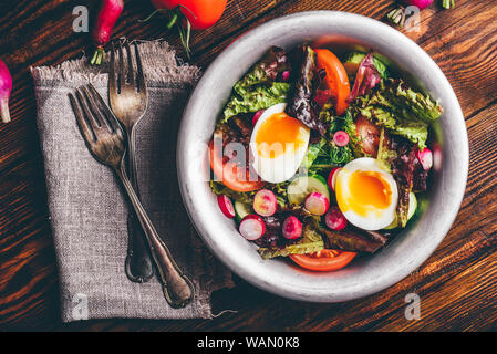 Fresh spring salad with tomato, radish, cucumber, red leaf lettuce and boiled eggs in metal bowl. View from above Stock Photo