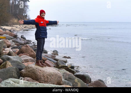 young man standing on sea stones, man on the seashore with his hands up, Baltic sea, Kaliningrad region, Russia, December 30, 2018 Stock Photo