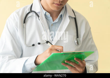 Closeup of asian male doctor writing health report,Medical care or prescription on the green clipboard in hospital. Concept of Medical and healthcare. Stock Photo