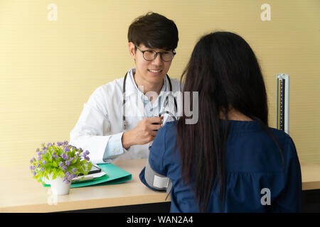 Handsome and young doctor giving a consultation to a patient and Explain medical informations and check blood Pressure in doctor office at hospital. C Stock Photo
