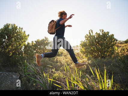 Active man jumping while hiking in mountains Stock Photo
