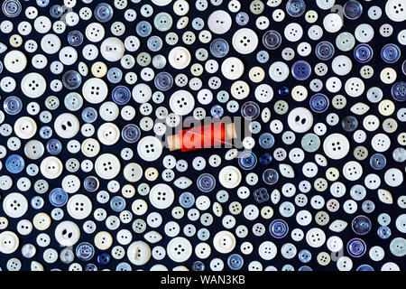 background - different light buttons and reel of red thread with needle on a dark surface Stock Photo