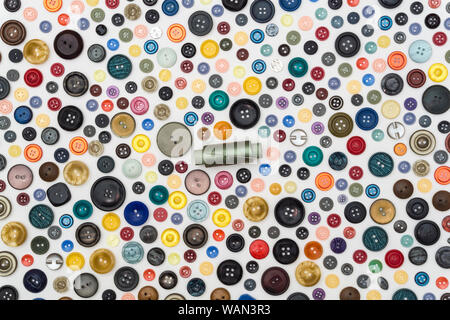 background - multicolored buttons and reel of green thread with needle on a white surface Stock Photo