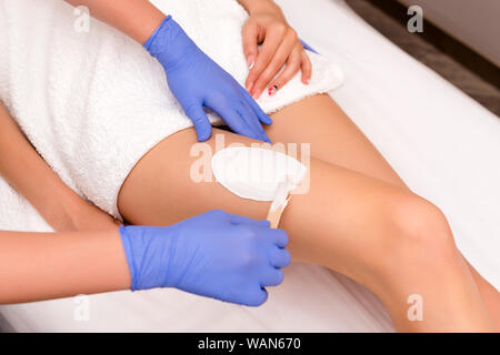 Beautician waxing female legs in spa center.Removing unnecessary hair on the legs. Procedure sugaring in a beauty salon. Sugar depilation. Depilatory Stock Photo