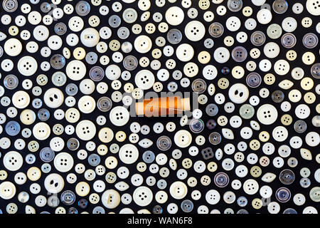 background - different light buttons and reel of yellow thread with needle on a dark surface Stock Photo