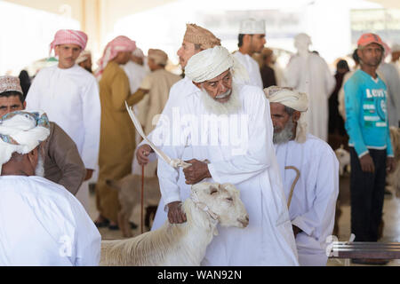 Man in traditional clothes wearing a head scarf taking a goat for sale at Sinaw market, Oman Stock Photo