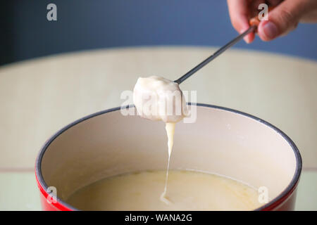 Swiss traditional dish - cheese fondue. Baguette on a fondue fork is being dipped in melted cheese. Served in a communal pot heated with a candle or spirit lamp. Close up picture. Stock Photo