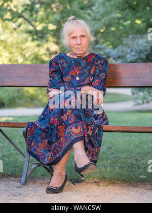 An elegantly dressed, elderly woman is sitting on a park benchis sitting on a park bench. Poland. Stock Photo