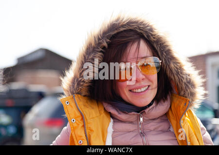 Cute Caucasian girl in yellow glasses, pink jacket, vest shows her hand on the city from the top of the mountain. Back view. Concept woman traveler, g Stock Photo