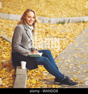 Woman sitting in autumn city park with golden trees around, looking at camera, image toned Stock Photo