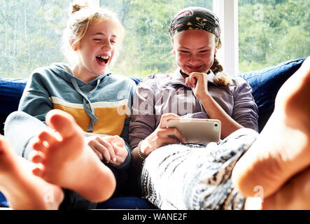 Young girls sitting on a couch looking at a screen and laughing Stock Photo