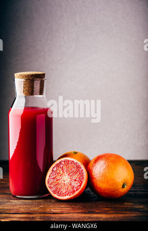 Bottle of blood orange juice with halved fruit on wooden table Stock Photo
