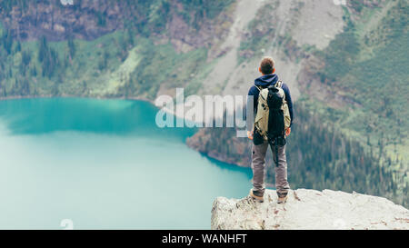 Male hiker is standing on a cliff looking at the lake in Glacier NP