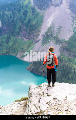 Hiker is standing on a cliff looking at the lake in GlacierNP, Montana