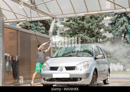 A man washes his car in a self-service sink in the summer outdoors. Stock Photo