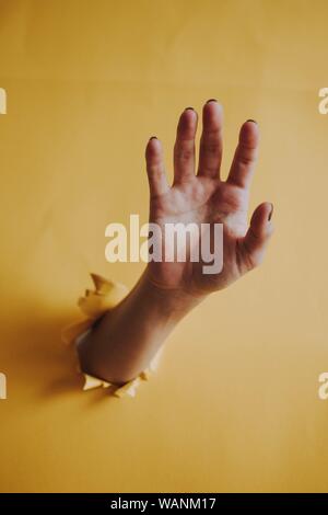 Vertical shot of a person's hand palm breaking through a yellow paper wall Stock Photo
