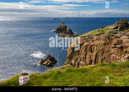 Sign for dangerous cliffs at the edge of Land's End looking to Armed Knight and Longships Lighthouse islands in the Atlantic Ocean Cornwall England Stock Photo