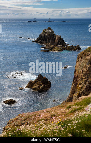 Cliff edge with Sea Thrift flowers at Land's End and Armed Knight and Longships Lighthouse islands in the Atlantic Ocean Cornwall England Stock Photo