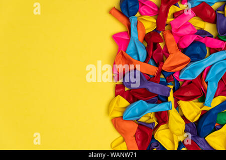 Close up view of colored deflated balloons. Top view of colored balloons on yellow background, with left copy space, flat lay. Great for birthday stor Stock Photo