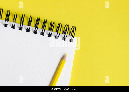 Corner of a spiral bound notepad / sketchpad on a yellow background, with a yellow pencil and space for copy Stock Photo