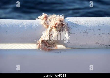 Broken rope tied in a knot around part of the old wooden paddle on the white boat with blue sea surface in the background and copy space Stock Photo