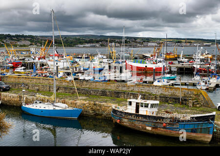 View of various boats moored at stone piers of Newlyn harbour with view of Penzance across Mounts Bay Cornwall England Stock Photo