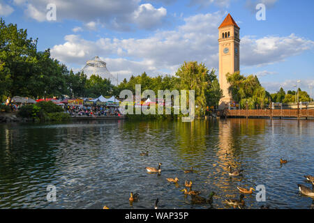 Festival goers enjoy the annual Pig out in the Park under the clock tower at Riverfront Park, as ducks swim in the Spokane River in Spokane Washington Stock Photo