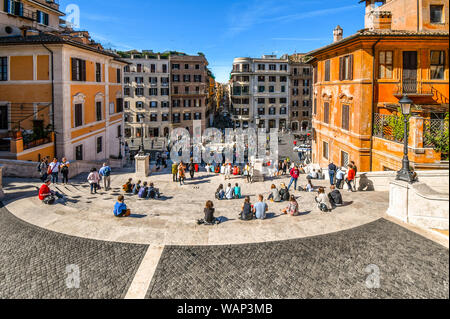 View of Via dei Condotti from the Spanish Steps under the Trinita dei Monti of tourists sitting on the steps, relaxing and enjoying Piazza di Spagna Stock Photo