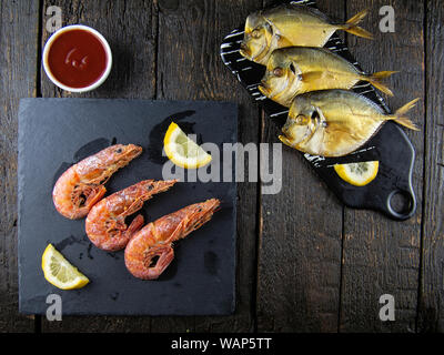 Boiled shrimps and smoked fish with lemons, greens and sauce on a wooden background. Top view Stock Photo