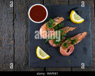 Boiled shrimps with lemons, greens and sauce on a wooden background. Top view Stock Photo
