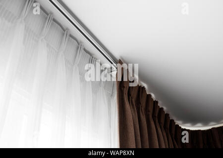 Brown curtains and white tulle on a rail with a white ceiling. Curtain interior decoration in living or sleeping room. Comfortable live in your own ho Stock Photo