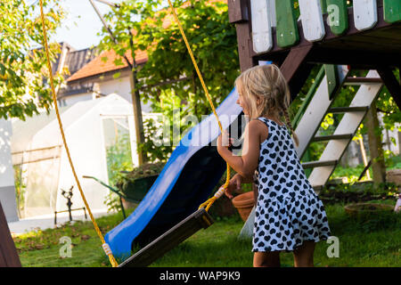 3-5 year old blond girl having fun on a swing outdoor. Summer playground. Girl swinging high. Young child on swing in garden Stock Photo