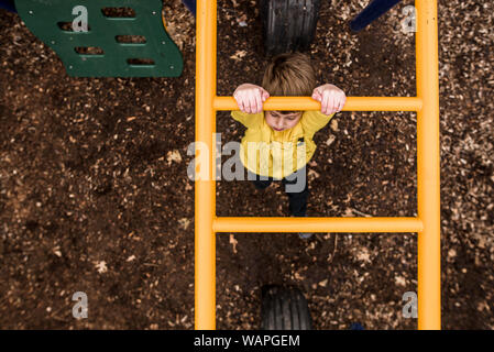 looking down on young boy going across monkey bars at playground Stock Photo