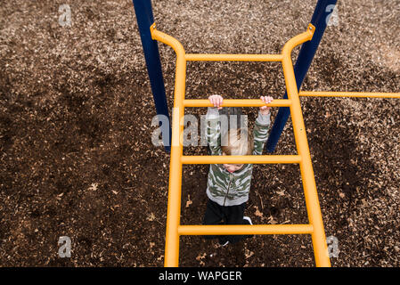 looking down from above at young boy going across monkey bars at park Stock Photo