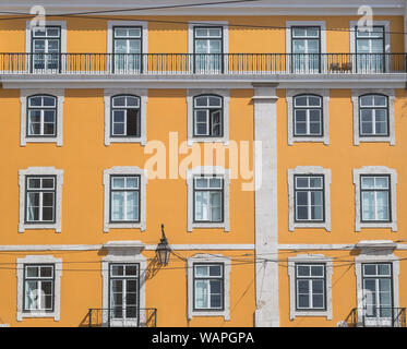 The outside of a typical building in Lisbon. Showing a bright yellow facade lots of windows and some balconies. Stock Photo